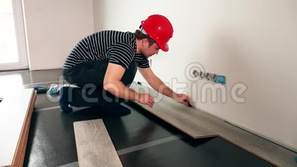 在新房子里安装木地板的戴红头盔的工人视频的预览图