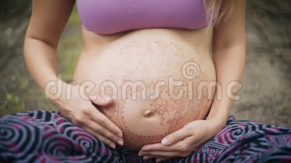 高加索孕妇长着波西米亚风格的长发大肚子上的白色麦亨迪新时代的宝宝期待视频的预览图