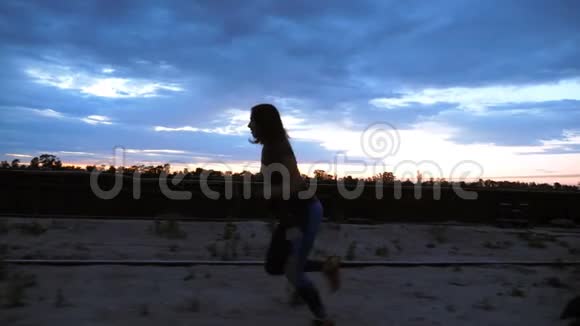 一个年轻的女人穿着运动服沿着货运港的沙墩慢跑在黎明的黄昏视图视频的预览图