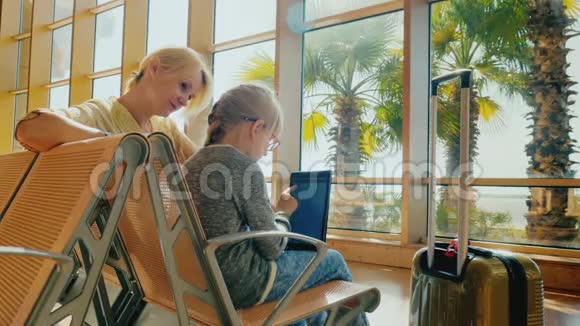 妈妈和女儿正在机场候机楼等待航班一个女孩在用平板电脑一个年轻的女人在坐视频的预览图