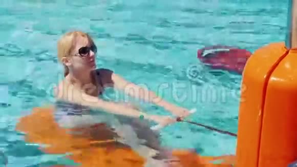 一位戴太阳镜的年轻女子正在游泳池里的模拟器上训练肌肉积极的户外活动视频的预览图
