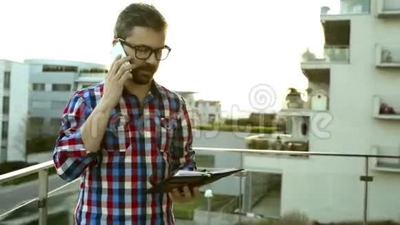有智能手机和私人组织者的商人站在阳台上视频的预览图
