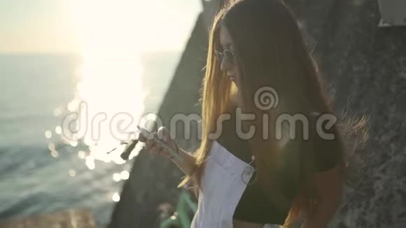 年轻漂亮的女人在日出或日落时使用智能手机在海边骑老式自行车视频的预览图