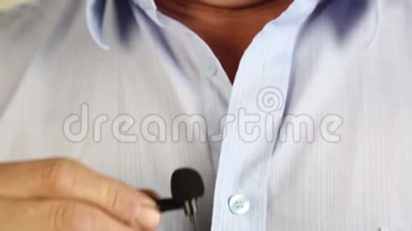 一个人把一个带扣眼的小麦克风固定在衬衫上视频的预览图