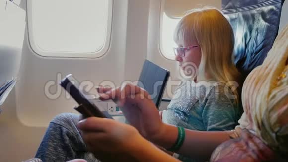 妈妈和女儿坐飞机用平板电脑和电话道路上的技术视频的预览图