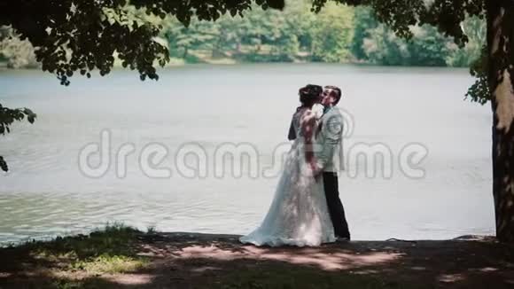 婚礼当天亲吻情侣的侧景幸福的新娘和新郎在河岸上美丽的地方视频的预览图