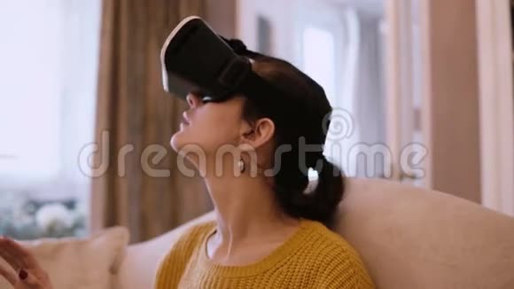 虚拟现实眼镜中年轻女子坐在家里沙发上的肖像女性在VR耳机里环顾四周视频的预览图