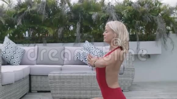 漂亮的女孩穿着红色泳衣练习瑜伽坐在热带地区房子的开阔走廊上视频的预览图