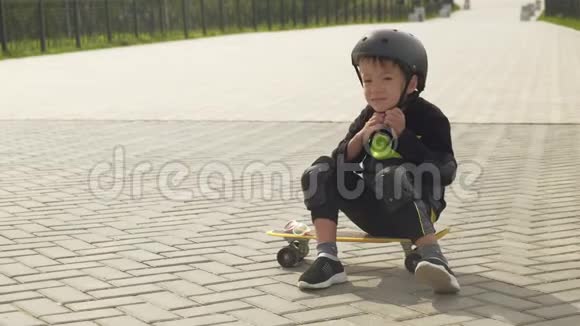 一个戴着保护头盔的学龄前男孩在公园里骑滑板夏季视频的预览图