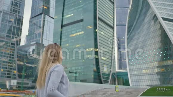 在摩天大楼和摩天大楼的背景下女孩心情很好地穿过市中心的城市视频的预览图