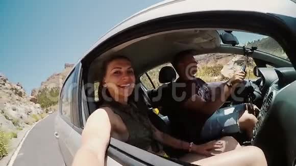 年轻夫妇在车里旅行美女拿着相机男人开车穿越岩石的情人视频的预览图