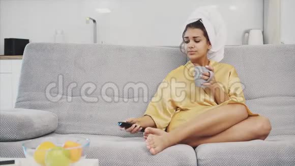 快乐的女人带着遥控器洗澡后休息时选择电视频道头上是一条毛巾视频的预览图