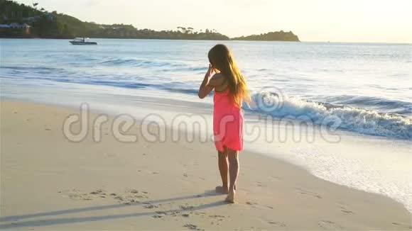 可爱的快乐小女孩在日落时在白色的海滩上嬉戏流动电视视频的预览图