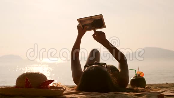 年轻的旅游女孩使用移动平板小工具和日光浴在热带天堂海滩4K慢动作普吉岛视频的预览图