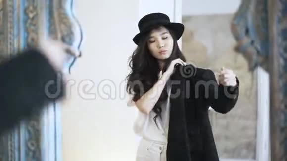 一位戴着帽子的亚洲时尚视频博主正在商店里试穿一件黑色外套视频的预览图