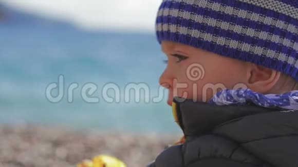 一个戴着冬帽的漂亮小孩子在沙滩上玩玩具视频的预览图