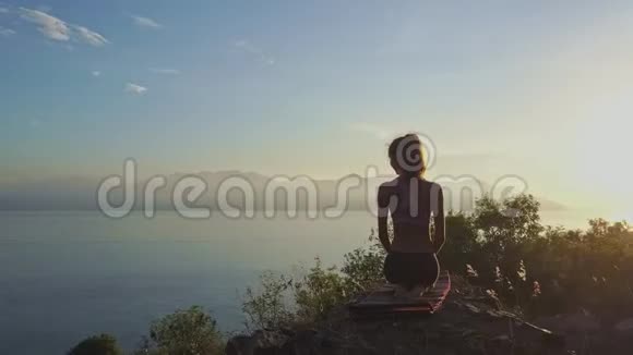 背部苗条的女孩坐在瑜伽姿势悬崖在黎明视频的预览图