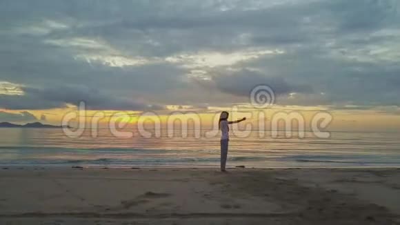 女孩让赛尔夫在沙滩上对抗海洋上的金色日出视频的预览图