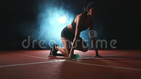 黑暗背景下的女运动员正准备从跑步机上的垫子上进行越野冲刺视频的预览图