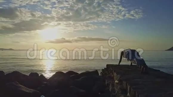 女孩剪影手持瑜伽姿势对抗海洋上空的日出视频的预览图