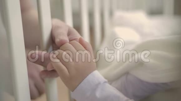 父母握着睡在婴儿床上的小孩子的手幸福的家庭和她的新生儿在一起这就是视频的预览图