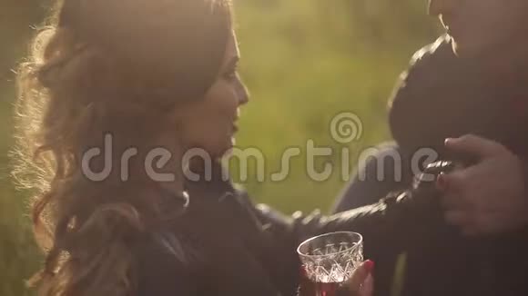 一对漂亮的情侣在野餐时穿着皮夹克相爱酒杯里的红酒日落时分在柔和的光线下视频的预览图