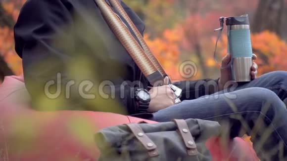 一个拿着相机的人坐在秋林里泡芙手里拿着一个热水瓶滑球射击视频的预览图