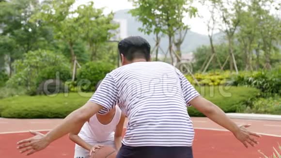 在花园里和爸爸一起打篮球时亚洲的儿子在做抽水假动作视频的预览图