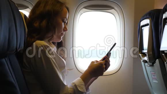 在飞机上浏览智能手机的年轻女性视频的预览图