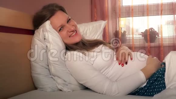 年轻快乐的孕妇抚摸她的腹部看着镜头视频的预览图