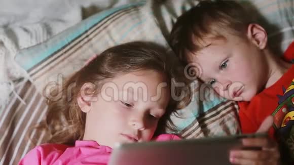 儿童一起躺在床上使用平板电脑的特写镜头女孩拿着平板电脑男孩看卡通视频的预览图