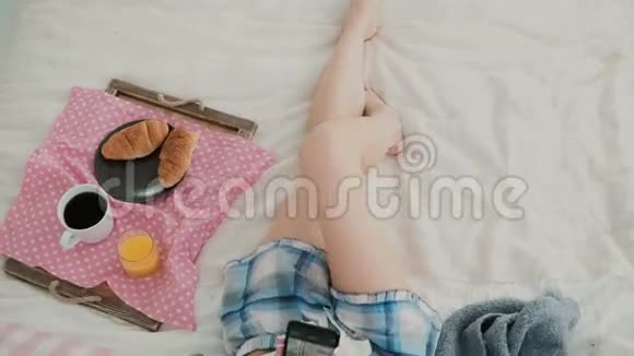 年轻的黑发女人躺在床上早餐时使用智能手机的漂亮女孩女性观看旅行照片视频的预览图