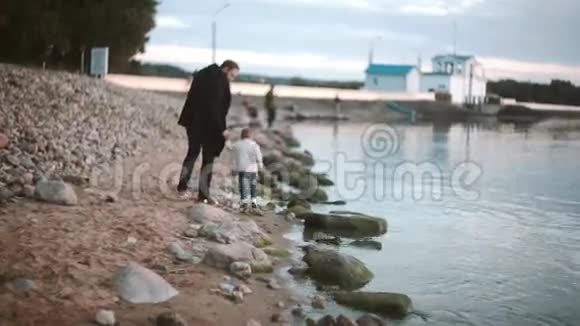 父亲和儿子在海滩上牵手在日落时沿着海岸散步女孩向男人跑去父亲拥抱女儿视频的预览图