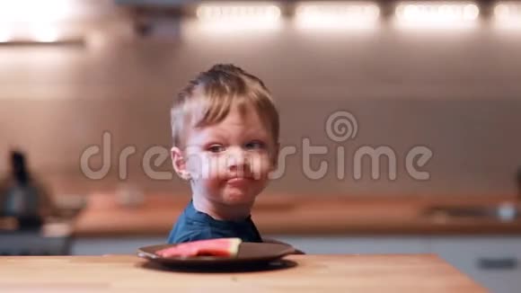 小男孩坐在桌子旁转过头看到盘子上的西瓜男欢叫一声咬一口视频的预览图
