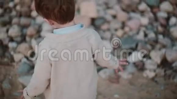 可爱的小男孩在石头附近的沙子上奔跑从一只脚移动到另一只脚在外面散步的男人视频的预览图