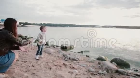 母亲和儿子在日落的岸边男孩把石头扔进水里男性转身摔倒露出猛犸的手视频的预览图