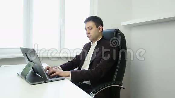 商人坐在桌子旁的办公椅上在银色的笔记本电脑上打字视频的预览图