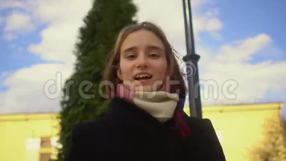 一个年轻漂亮的时髦女孩在一棵针叶树一座黄色建筑和一座蓝色建筑的背景下与交谈视频的预览图