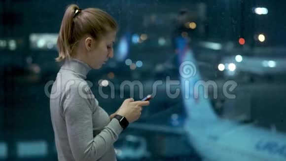 女旅行者等着出发用她的手机一个年轻的女孩写了一条信息等待航班视频的预览图