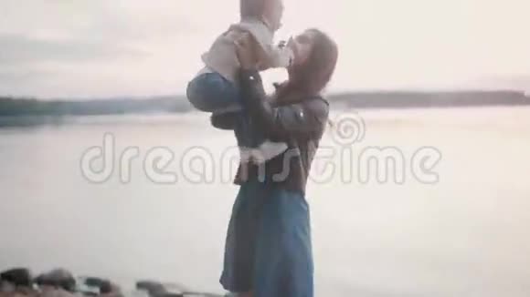 母亲牵着儿子的手在海滩的岸边微笑的女人抱起她的小男孩亲吻拥抱视频的预览图