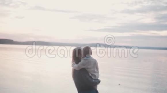 年轻的黑发女人抱着小男孩在海滩海岸母亲吻她的儿子用手指指着地平线视频的预览图