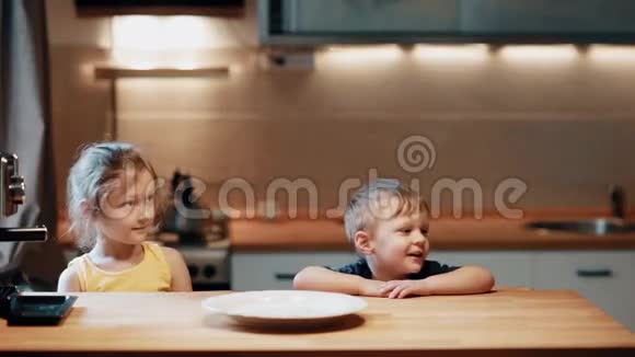 哥哥姐姐坐在桌子旁妈妈带着西瓜放到桌子上男孩和女孩碰水果视频的预览图