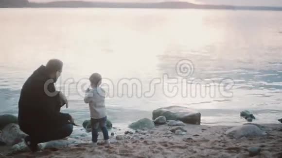 年轻人蹲在岸边和小男孩说话而不是站起来父子俩在一起度过时光视频的预览图