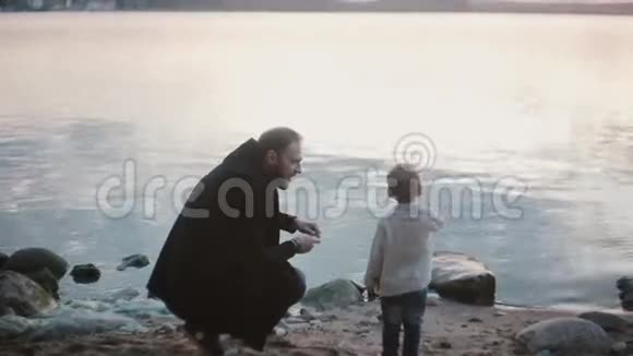 父子在岸边交谈男人蹲着教男孩如何玩跳绳小男孩高兴地跳着视频的预览图
