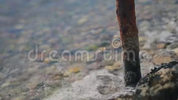 海浪拍打和退去在岩石海滩生锈的管子上视频的预览图