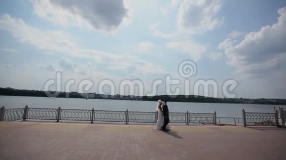 结婚舞会新婚夫妇正在海滨散步新娘和新郎走在风景如画的蓝色湖泊附近视频的预览图