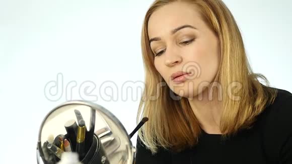 美丽的女人在小镜子前画眉毛用化妆刷做日常化妆慢动作视频的预览图