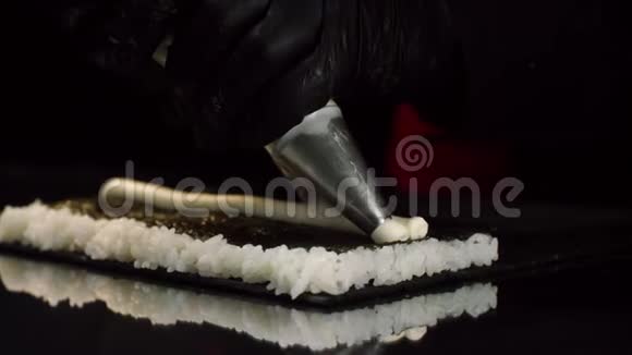制作卷式寿司过程的特写手套中的厨师从面皮袋中将奶油填充到床单上视频的预览图