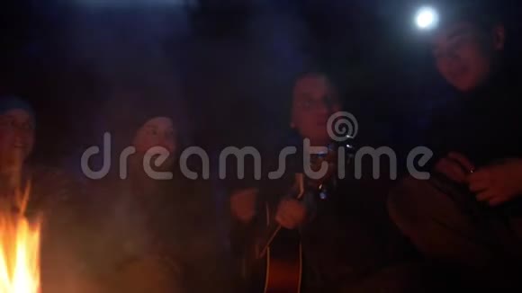 在夜晚森林的篝火旁唱着歌弹着吉他的年轻快乐的朋友视频的预览图