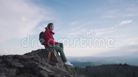 一个女孩在山里旅行的肖像坐在悬崖边上的岩石上休息的年轻女子视频的预览图